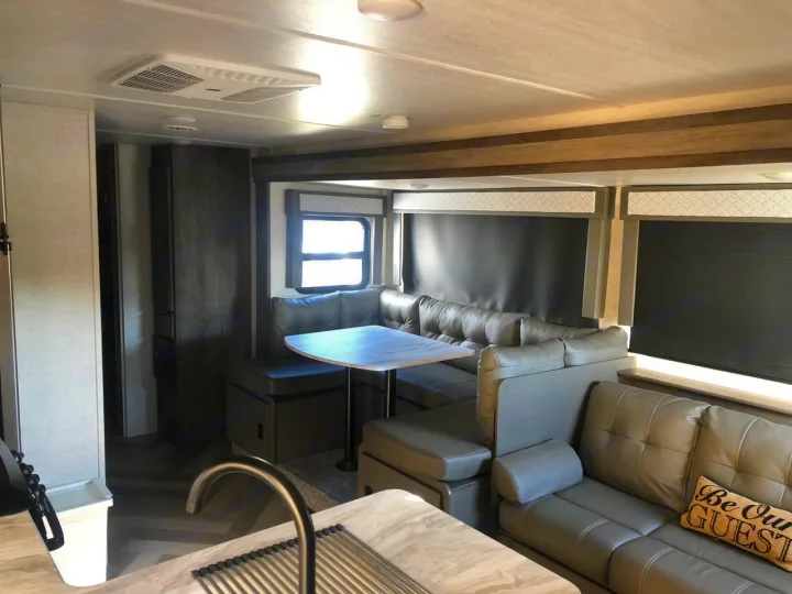Modern RV rental interior: kitchen, U-shaped dinette, comfortable sofa, and large windows create a cozy living space.. Forest River Wildwood 2020