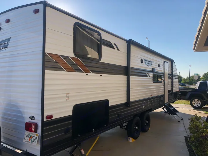 This bright white and brown travel trailer is set up, likely an RV rental. Parked on concrete with stairs down for access.. Forest River Wildwood 2020