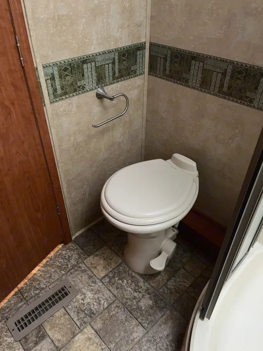 Compact RV rental bathroom with a Dometic toilet, decorative wall, toilet paper holder, tiled floor, and a floor vent.. Forest River Georgetown M373DS 2011