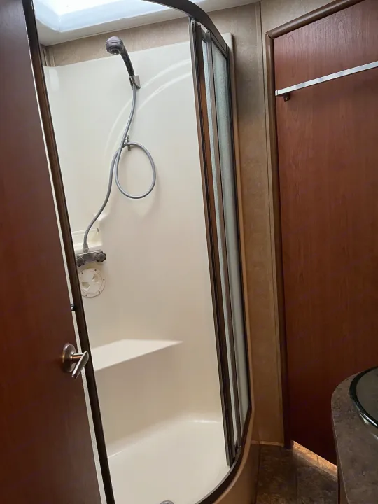 Inside an RV rental: a bright, compact bathroom shower with a hand-held showerhead and glass door.. Forest River Georgetown M373DS 2011