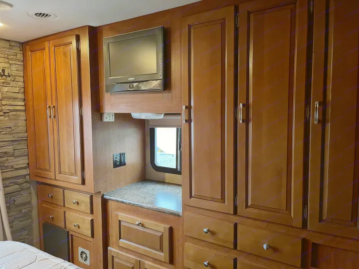 Inside this RV rental: bedroom area featuring a wall-mounted TV, numerous wood cabinets & drawers, plus a window.. Forest River Georgetown M373DS 2011
