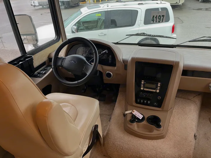 Step inside this RV rental! Driver's cockpit with Ford steering wheel, dashboard, and cream leather seat.. Forest River Georgetown M373DS 2011