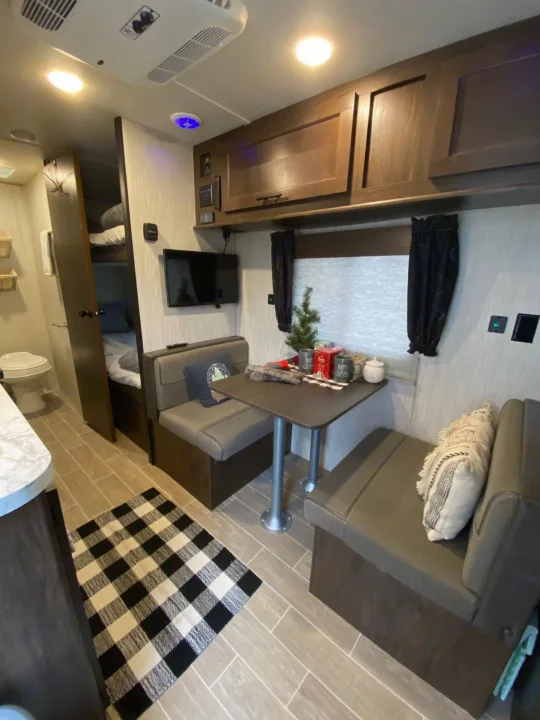 View of a modern rv rental interior: dinette seating, kitchenette, bunks, & bathroom entrance. Ready for adventures!. Forest River Wolf Pup 2021