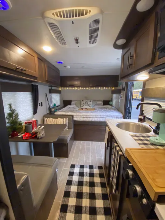 Explore this cozy RV rental's interior, featuring a compact kitchen, dinette, and comfortable bed. Plaid accents.. Forest River Wolf Pup 2021