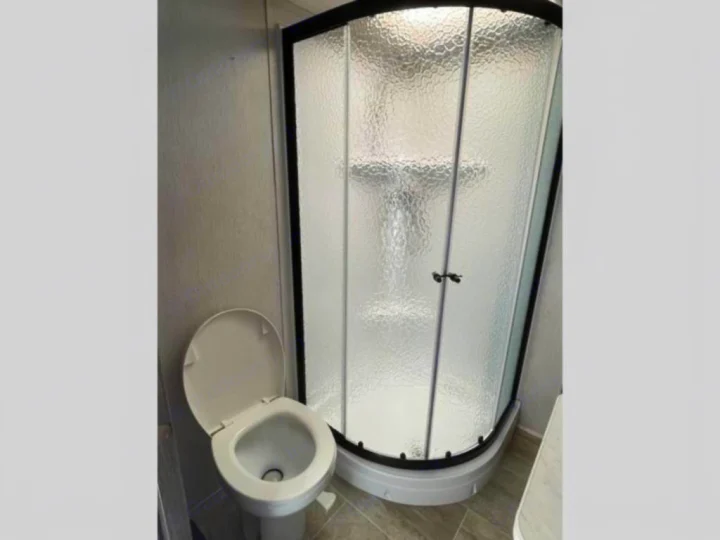 RV rental bathroom: compact design with a white toilet (seat up) and a curved, frosted glass shower enclosure.. Heartland RVs Pioneer 2020