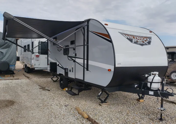 This white and gray Wildwood FSX travel trailer is an ideal rv rental, set up on a gravel lot with its awning extended.. Forest River Other 2022