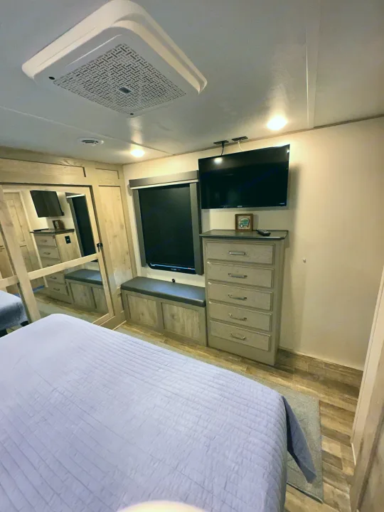 Cozy RV rental bedroom with a purple-quilted bed, TV, dresser, window seating, and ceiling AC unit.. Keystone RV Alpine 2022