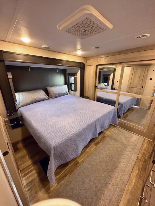 Comfortable RV rental bedroom featuring a bed with light blue quilt, mirrored closet, and wood flooring for mobile living.. Keystone RV Alpine 2022