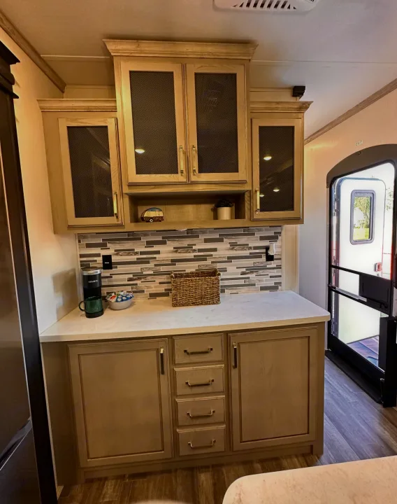 RV rental kitchen: cozy camper galley with light wood cabinets, tiled backsplash, and exit door.. Keystone RV Alpine 2022