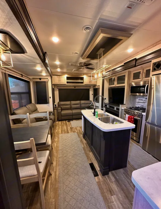 Modern RV rental with a spacious interior: kitchen island, dining table, and living area with recliners and sofa.. Keystone RV Alpine 2022