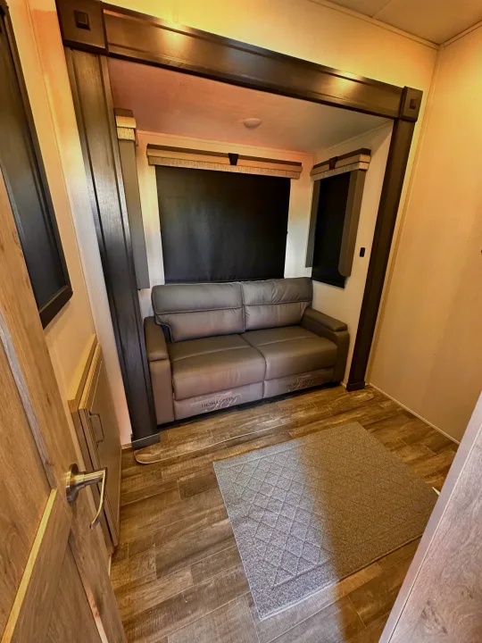RV rental: cozy slide-out living space with gray sofa, wood-look floor, & window blinds. Compact camper interior.. Keystone RV Alpine 2022