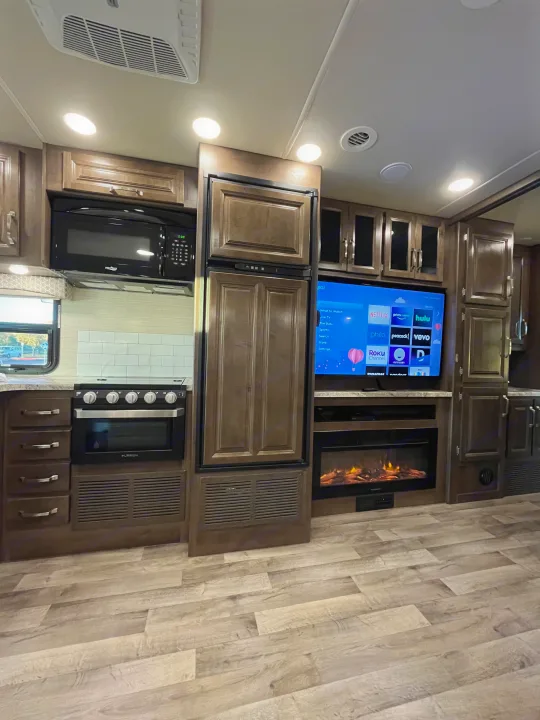 Modern RV rental interior: kitchen with microwave, oven, fridge; living space with TV, fireplace, wood floors.. Jayco Greyhawk 2020