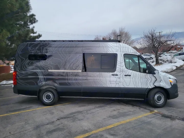 Custom Mercedes-Benz Sprinter van rv rental, featuring unique topographic map graphics, parked on an asphalt lot.. Mercedes-Benz Sprinter 2022