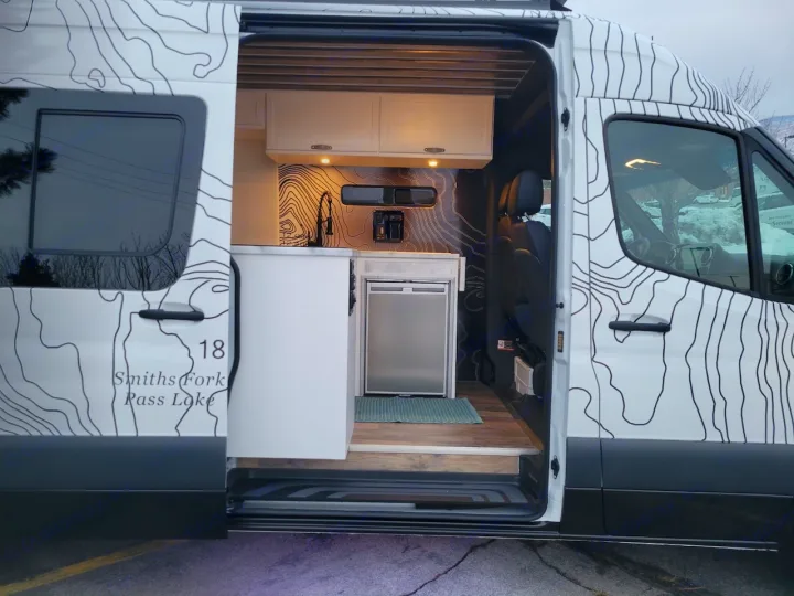 Explore this RV rental's custom camper van interior, featuring a compact kitchen with a sink & fridge.. Mercedes-Benz Sprinter 2022