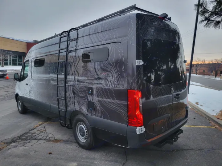 Explore in style: This dark custom topographic-wrapped RV rental van features a roof rack and side ladder for adventure.. Mercedes-Benz Sprinter 2022