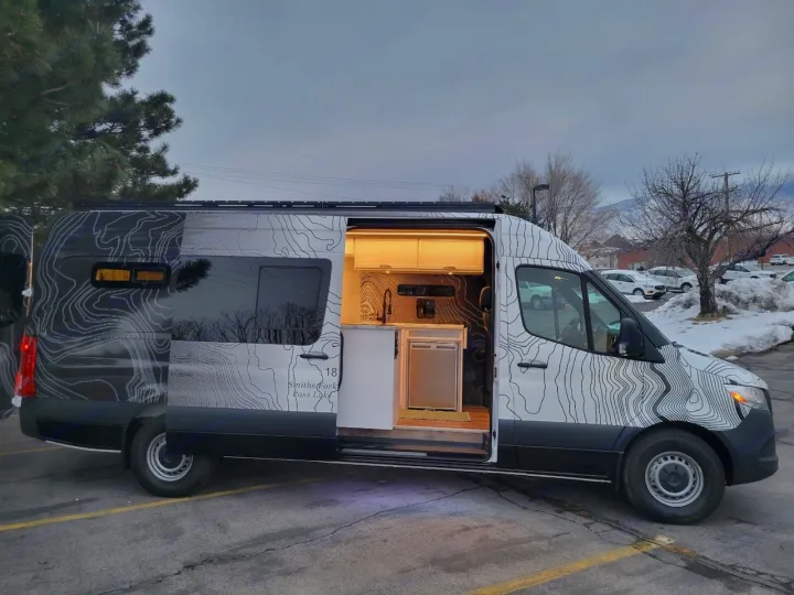 Custom van RV rental with open side door revealing a mobile kitchen, cabinets & unique topographical map design.. Mercedes-Benz Sprinter 2022