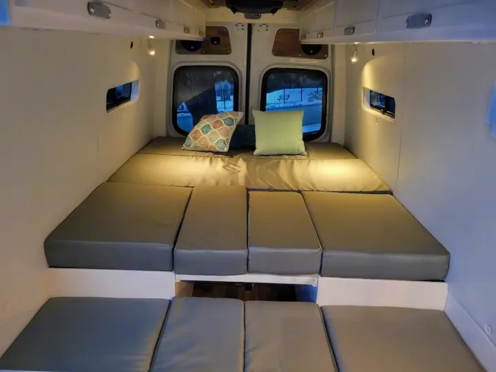 Comfortable camper van interior for your next RV rental adventure. Features modular grey bed cushions & cozy lighting.. Mercedes-Benz Sprinter 2022