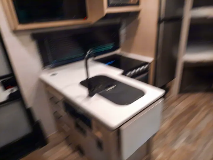 This blurry photo shows an RV rental kitchen: white counters, dark sink, cooktop, and light cabinets. Perfect for mobile living.. Forest River Rockwood Mini Lite 2021