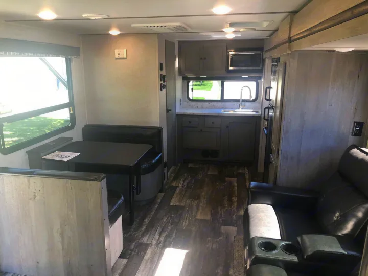 Spacious RV rental interior with a cozy dining area, fully equipped kitchen, and comfortable recliners on wood-look flooring.. Keystone RV Outback Ultra-Lite 2019