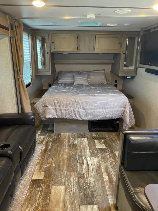 An RV rental's compact bedroom and living area, with a comfy bed, sofa, and overhead storage, ready for your next trip.. Keystone RV Outback Ultra-Lite 2019