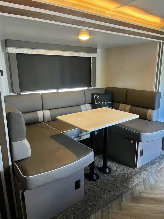 Comfortable RV rental dinette featuring U-shaped gray seating, a light table, and window blind.. Forest River Wildwood X-Lite 2022