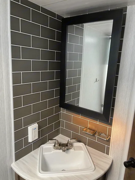 Compact RV rental bathroom with dark gray subway tile, white sink, and black-framed mirror, ideal for travel comfort.. Forest River Wildwood X-Lite 2022