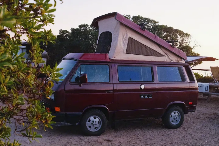 A maroon pop-top VW camper van, ideal for an RV rental adventure, parked at dusk with its roof extended and hatch open.. Volkswagen Westfalia 1990