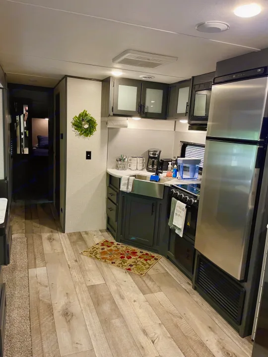 Explore this modern RV rental kitchen & living space! Features stainless appliances, dark cabinetry, wood-look floors, and cozy decor.. Dutchmen Aspen Trail 2022
