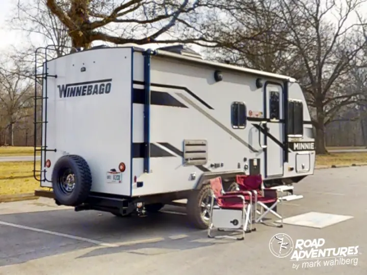 Enjoy an RV rental experience! This white Winnebago Minnie travel trailer is set up with chairs and a cooler in an outdoor park.. Winnebago Micro Minnie 2100BH 2023