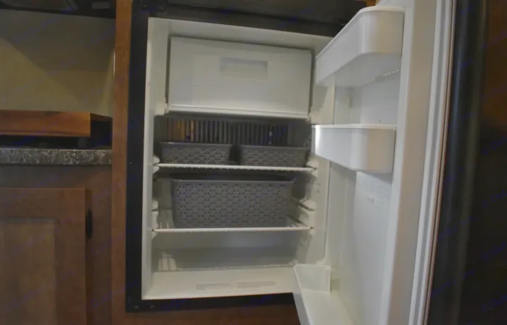 Open RV rental refrigerator showing freezer, shelves with gray storage baskets, and door compartments.. Starcraft Autumn Ridge Mini 2017
