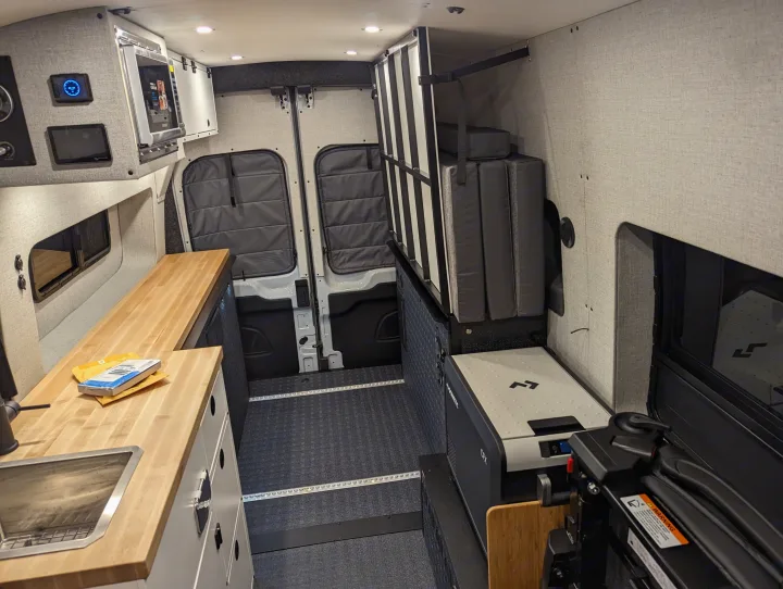 Spacious rv rental interior featuring a compact kitchenette with sink, microwave, foldable bed, and Dometic fridge.. Grit Overland GO A/T 2022
