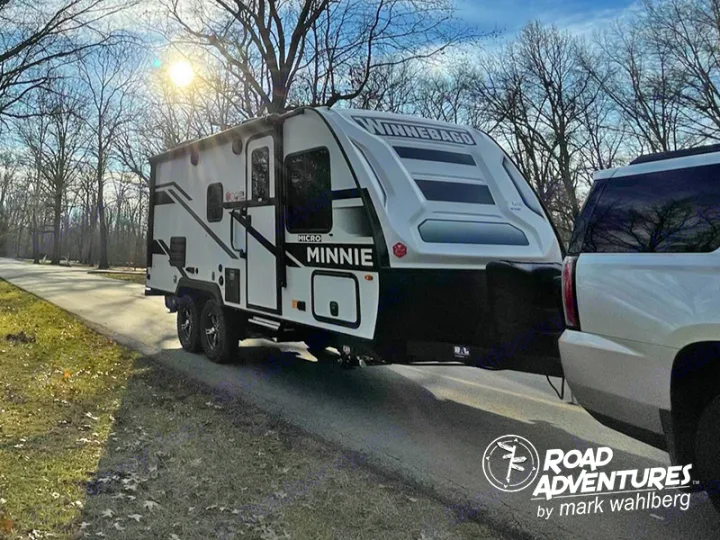Winnebago Micro Minnie RV rental travel trailer being towed by a white SUV on a clear day with bare trees in the background.. Winnebago Micro Minnie 2100BH 2023
