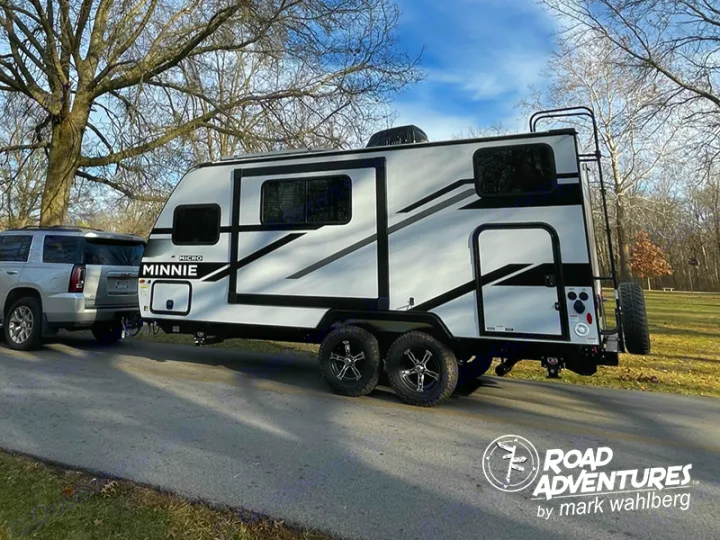 A white Micro Minnie travel trailer, ideal for an rv rental, hitched to an SUV on a paved road, ready for outdoor adventure.. Winnebago Micro Minnie 2100BH 2023