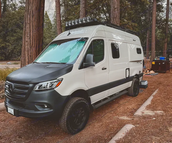 Explore in style with this Revel camper van RV rental, ready for adventure at a forest campsite. A dog relaxes nearby.. Other Revel 2023