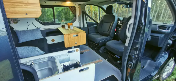 Inside an RV rental: a modern camper van interior showing a kitchen, convertible seating, and front cabin.. Renault Trafic 2023