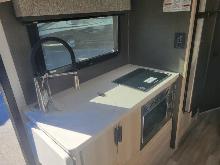 Inside an RV rental, a compact kitchenette features a sink, Dometic stovetop, Greystone microwave, and controls. Ready for travel!. Forest River Forester 2023
