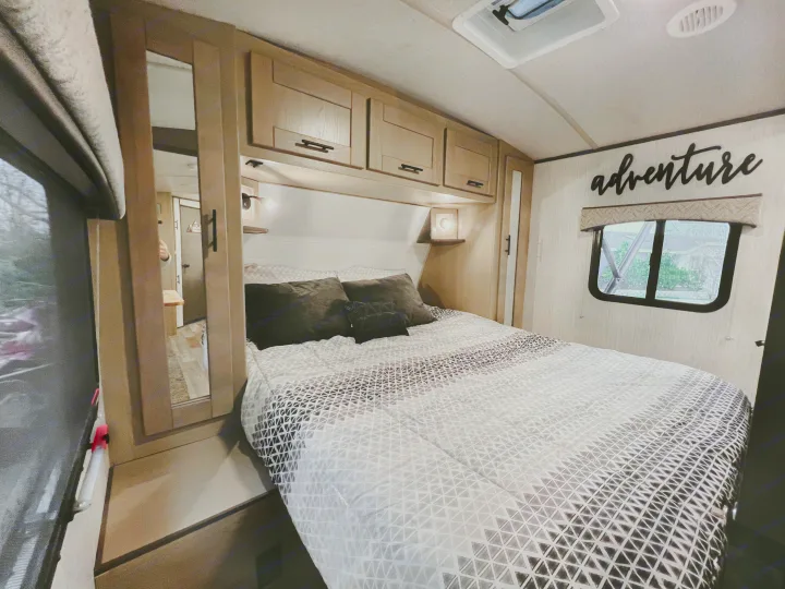 Cozy RV rental bedroom with a patterned comforter, overhead cabinets, and "adventure" wall decor.. Heartland RVs Sundance Ultra Lite 2021