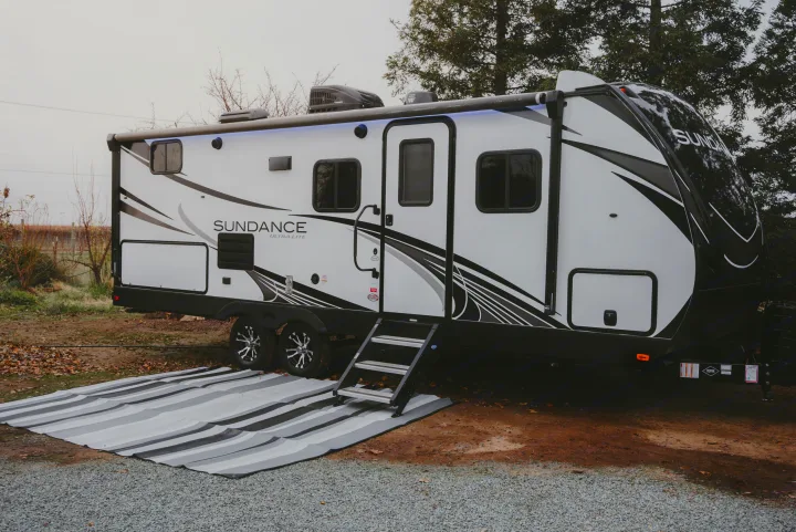 Sleek white & black Sundance Ultra Lite travel trailer RV rental, parked outdoors with its awning deployed & ground mat.. Heartland RVs Sundance Ultra Lite 2021