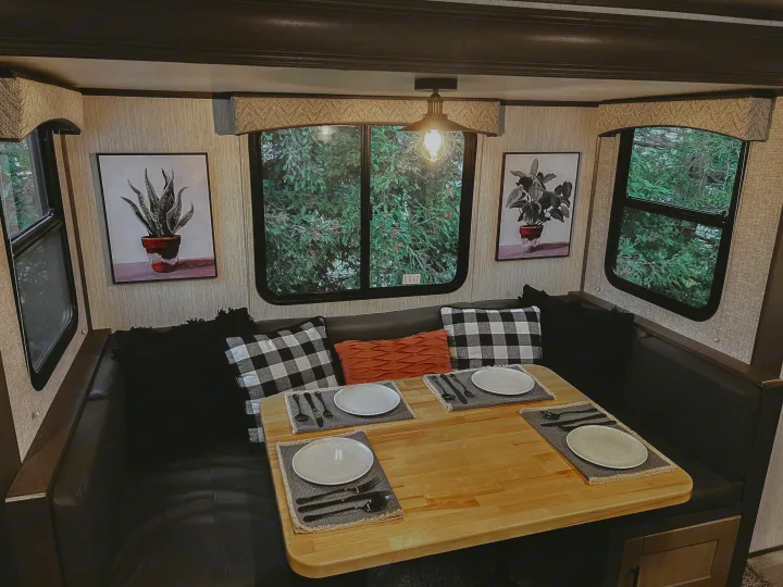 This RV rental's cozy dinette offers U-shaped leather seating, a wooden table set for four, and plant artwork by large windows.. Heartland RVs Sundance Ultra Lite 2021