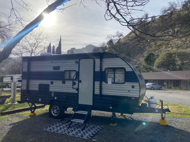Sunny view of a compact Wolf Pup RV rental, set up at a gravel campsite with stabilizers & mat.. Forest River Wolf Pup 2021