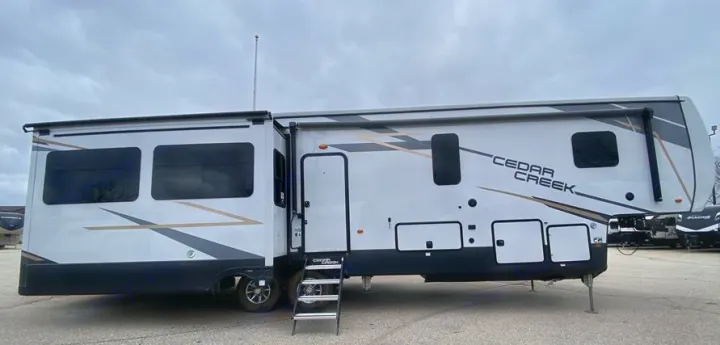 Large white Cedar Creek fifth-wheel RV rental, parked on asphalt. Features multiple slide-outs, tinted windows, and entry steps.. Forest River Other 2022
