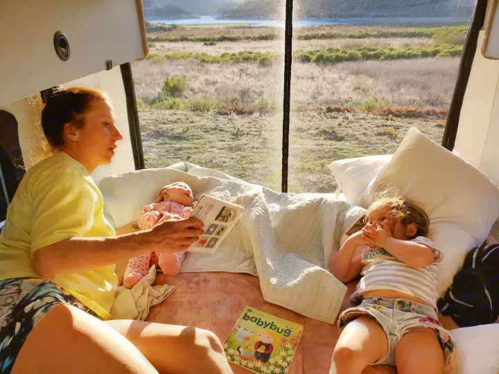 Cozy family moment inside an RV rental: Mom reads to her "baby" doll, while a toddler relaxes by the window overlooking nature.. Winnebago Solis 2021