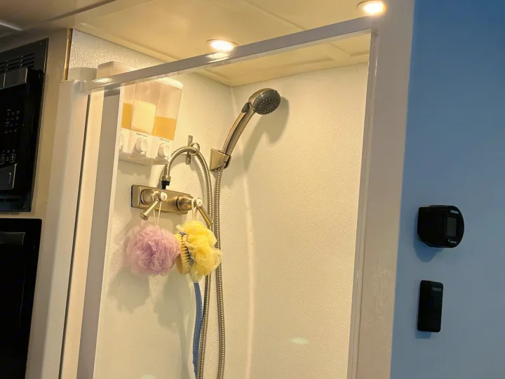 Compact RV rental shower featuring wall-mounted soap dispensers, loofahs, and shower controls for a convenient travel experience.. Ram Promaster 2022