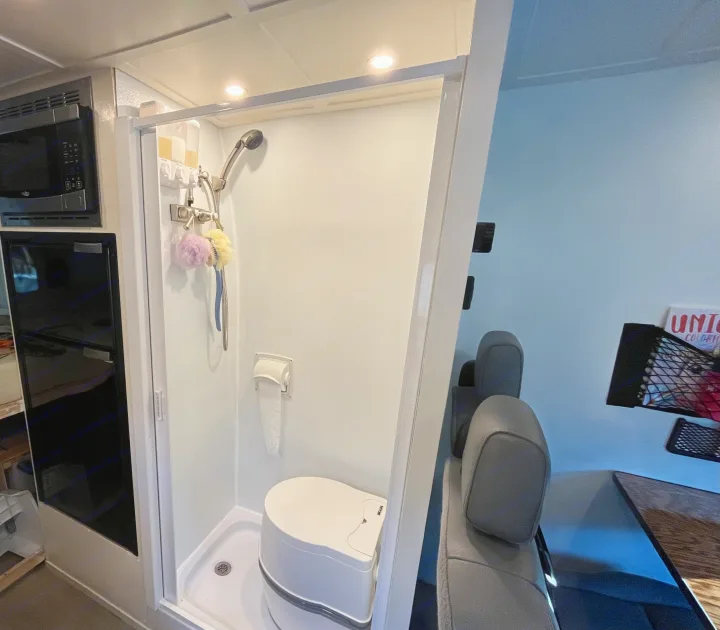 RV rental interior: compact wet bath with shower and portable toilet. Adjacent microwave and mini-fridge.. Ram Promaster 2022