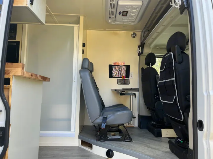 Spacious RV rental interior featuring a multi-functional living area with swiveling seats, fold-down table, and a compact shower stall.. Ram Promaster 2022