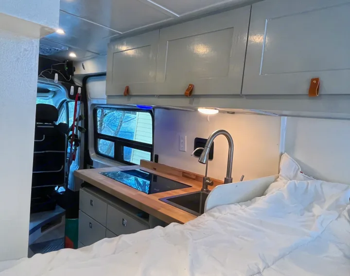 Inside an rv rental: functional kitchenette with cooktop & sink, comfy bed, and ample overhead cabinets.. Ram Promaster 2022