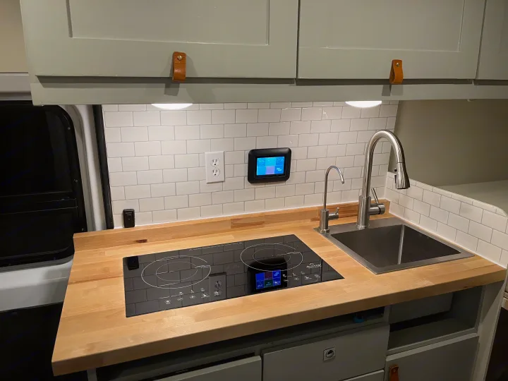 RV rental kitchen with wood counters, induction cooktop, sink, subway tile backsplash & smart system display.. Ram Promaster 2022