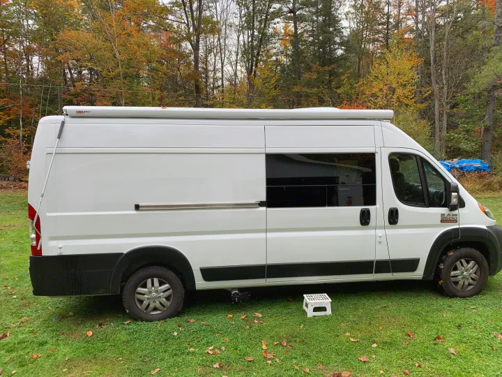 White Ram ProMaster camper van, ideal for rv rental adventures, parked on grass amidst autumn trees.. Ram Promaster 2022
