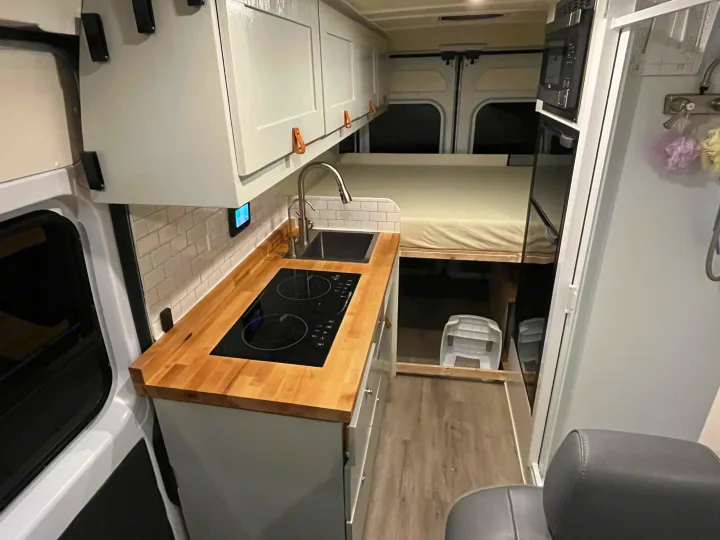 This RV rental's modern interior features a sleek kitchen with cooktop and sink, a raised bed, and smart storage.. Ram Promaster 2022