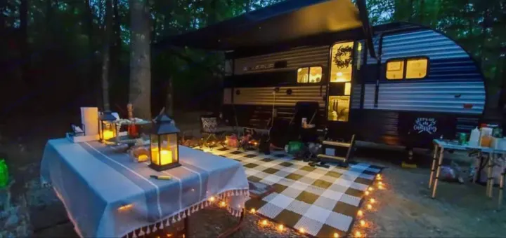Cozy RV rental at a nighttime campsite, featuring an illuminated outdoor rug, picnic table, and warm lanterns for a perfect camping trip.. Forest River Cherokee Wolf Pup 2022